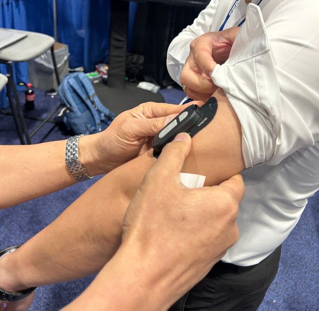 A close-up image of a person carefully applying Epicore Biosystems' Connected Hydration wearable device onto a tradeshow attendee's upper arm.